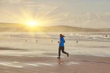 Genç bir kadın, Fas 'ın Essaouira sahilinde serinletici bir koşunun keyfini çıkarırken, dalgalar kıyı zeminine hafifçe vuruyor.