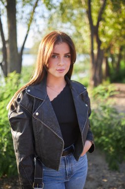 Deri ceket giymiş genç bir esmer, doğanın nefes kesici güzelliğinin arka planına karşı duruyor..