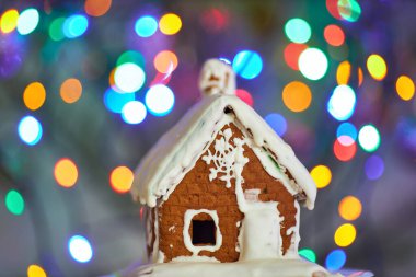 Beyaz kremayla kaplı bir zencefilli kurabiye evinin yakın plan çekimi arka planda neşeli bir bokeh etkisi yaratıyor..