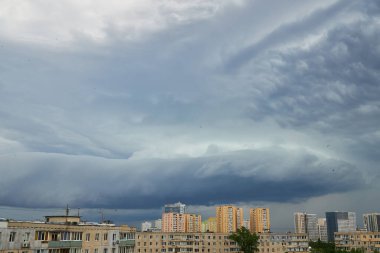 Yükselen bulutlar ve yumuşak akşam ışıklarıyla dolu bir gökyüzünün altında huzurlu bir şehir. Binalar dramatik bulut oluşumlarıyla tezat oluşturarak barışçıl ama dinamik bir şehir manzarası yaratıyor..