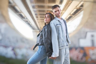 Arka planda büyük bir köprüyle dışarıda poz veren genç ve şık bir çift..