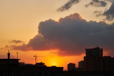 Bir inşaat vinci ve binalar çarpıcı kırmızı ve turuncu gün batımı gökyüzüne karşı siluetlendi. Günbatımının sıcak renkleri, karanlık kentsel yapılarla çarpıcı bir tezat oluşturur..