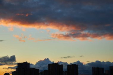 Karanlık bulutlar ve turuncu röflelerle dolu canlı bir günbatımı gökyüzü şehrin ufuk çizgisine zıt düşüyor. Kasvetli atmosfer, değişen bir gökyüzünün şehir manzarası üzerindeki güzelliğini yakalıyor..