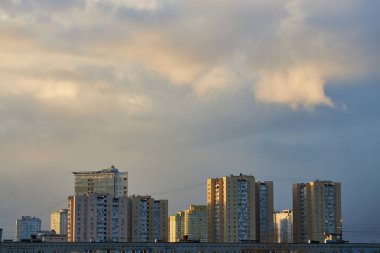 Karanlık bulutlar ve turuncu röflelerle dolu canlı bir günbatımı gökyüzü şehrin ufuk çizgisine zıt düşüyor. Kasvetli atmosfer, değişen bir gökyüzünün şehir manzarası üzerindeki güzelliğini yakalıyor..