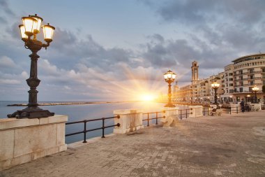 Bari, İtalya 'da deniz önü ve gezinti güvertesinde boş bank ve lamba direkleri. Romantik, sakin, rahatlatıcı bir akşam. Güneş batıyor.