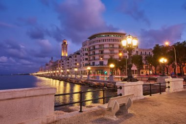 Bari, İtalya 'da deniz önü ve gezinti güvertesinde boş bank ve lamba direkleri. Romantik, sakin, rahatlatıcı bir akşam. Güneş batıyor.
