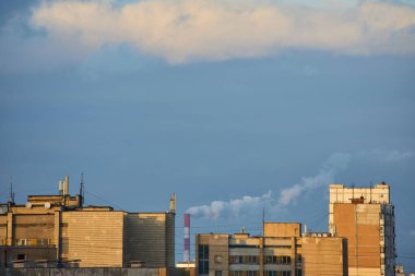 Bir şehir silueti gün batımında sıcak, altın bir ışıltıyla yıkanır. Gökyüzü yumuşak, altın bulutlarla dolu. Uzak binalara ve çatılara huzur dolu bir ışık saçıyor..