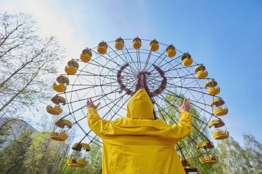 Sarı takım elbiseli yalnız bir araştırmacı Pripyat 'ın terk edilmiş lunaparkındaki dönme dolabın önünde duruyor. Çernobil Yasaklama Bölgesi' nin dokunaklı bir görüntüsü..