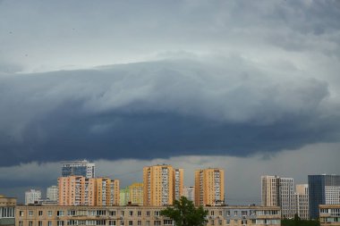 Yükselen bulutlar ve yumuşak akşam ışıklarıyla dolu bir gökyüzünün altında huzurlu bir şehir. Binalar dramatik bulut oluşumlarıyla tezat oluşturarak barışçıl ama dinamik bir şehir manzarası yaratıyor..