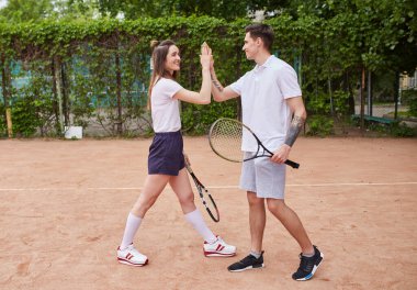 Bir erkek ve bir kadın tenis kortunda tebrik jestini paylaşıyor, internette içten bir gülümsemeyle. Ayar, sportmenliğin neşeli bir anını yakalıyor.