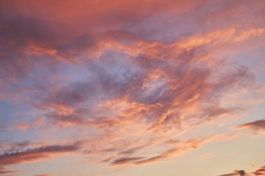 Akşam gökyüzünde turuncu, pembe ve mor sıcacık renklerle baş döndürücü bir günbatımı. Aydınlatılmış bulutlar, arka plan olarak kullanılmak üzere sakin ve atmosferik bir manzara yaratıyor..