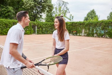 Bir erkek ve bir kadın tenis kortunda tebrik jestini paylaşıyor, internette içten bir gülümsemeyle. Ayar, sportmenliğin neşeli bir anını yakalıyor.