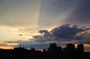 Gün batımında bir kuş sürüsü şehir manzarasının üzerinde uçar. Gökyüzü yumuşak pastel tonlarla boyanır, maviden pembeye dönüşür, kentsel binalar üzerinde sakin bir atmosfer yaratır.