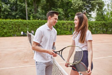 Bir erkek ve bir kadın tenis kortunda tebrik jestini paylaşıyor, internette içten bir gülümsemeyle. Ayar, sportmenliğin neşeli bir anını yakalıyor.