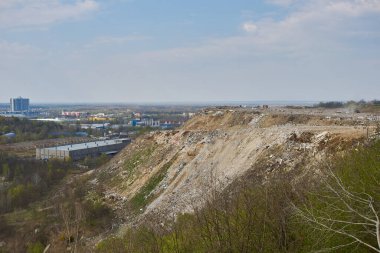 Arkasında büyük bir enkaz yığını, toprak yollar ve sanayi binaları olan bir inşaat atığı manzarası.