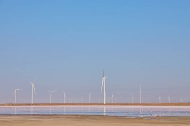 Rüzgâr türbinleri Ukrayna 'da açık mavi bir gökyüzünün altında tuz gölünün kıyısında temiz enerji üretiyor..