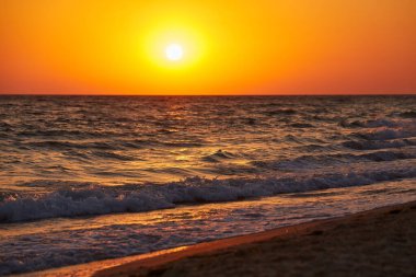 Hafif dalgalar canlı bir altın gün batımı sırasında kumlu bir plajda kıyıya vuruyor. Doğal fotoğraf, sıcak tonlar, arka plan için uygun..