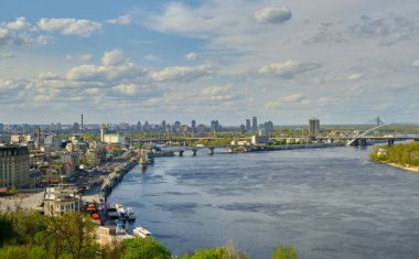 Ukrayna 'nın başkenti Kyiv' in panoramik görüntüsü, Dnipro Nehri 'ni, birkaç köprüyü ve şehrin ufuk çizgisini gözler önüne seriyor. Tarihsel Podil ilçesi ön planda görünür..