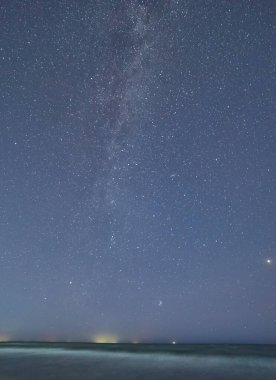Samanyolu Galaksisi, sakin bir deniz ve kıyı şeridinin üzerindeki gece gökyüzünde görünür..