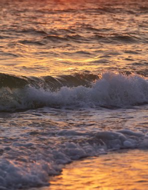 Dalgalar okyanusun üzerinde canlı kırmızı bir günbatımının altında kıyıya doğru yuvarlanıyor. Doğal, düzenlenmemiş fotoğraf..