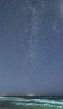 Samanyolu Galaksisi, sakin bir deniz ve kıyı şeridinin üzerindeki gece gökyüzünde görünür..