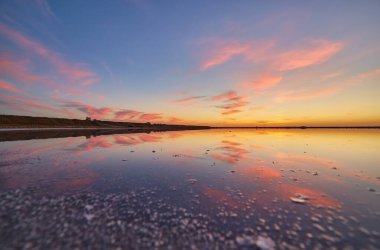 Pembe ve turuncu bulutlarla canlı günbatımı tuzlu gölün sakin ve sığ sularında yansıyor..