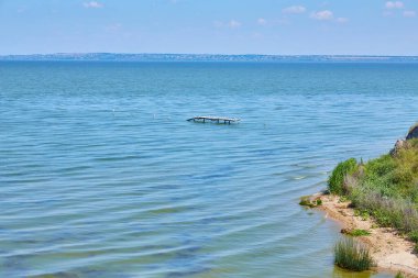 Uçsuz bucaksız, aşınmış sahil kayalıkları berrak mavi bir gökyüzünün altında sakin denizle buluşuyor..