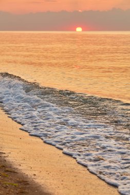 Denizin üzerinde gün doğumu, kumlu bir sahili ve sahil kayalıklarını aydınlatıyor..