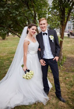 Gelin ve damat gün batımında romantik bir anı paylaşıyorlar. Resmi takım elbiseli damat, geline yakın duruyor. Beyaz bir elbise ve akarsu peçesiyle, altın güneş ışığıyla aydınlatılıyor..