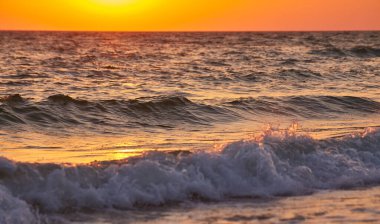 Okyanus dalgaları canlı bir altın gün batımında kıyıya çarpıyor. Doğal fotoğraf, sıcak tonlar, arka plan için uygun..