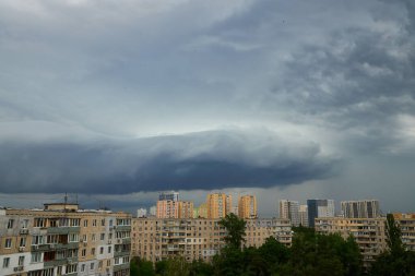 Büyük fırtına bulutları şehrin silueti üzerinde toplanarak karanlık, dönen gökyüzü ile aşağıdaki yüksek binalar arasında çarpıcı bir kontrastlık yaratır. Sahne yaklaşan fırtınanın şiddetini yakalıyor..