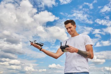 Beyaz tişörtlü bir adam, deniz kenarında manzaralı bir şehir geçmişine sahip bir yerde dururken uzaktan kumandalı uçak kullanıyor.