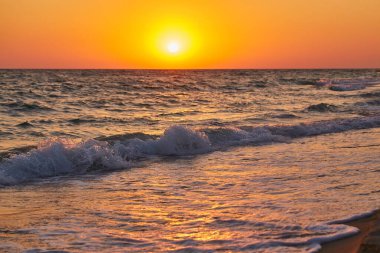 Okyanus dalgaları canlı bir altın gün batımında kıyıya çarpıyor. Doğal fotoğraf, sıcak tonlar, arka plan için uygun..