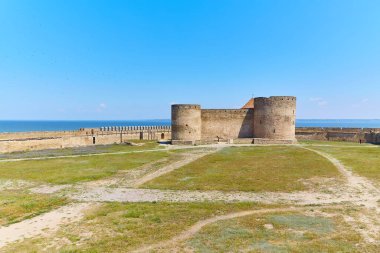 Akkerman Kalesi 'nin (Bilhorod-Dnistrovskyi Kalesi) taş duvarlarının ve kulelerinin manzarası, açık mavi gökyüzünün altında deniz görülebilir..