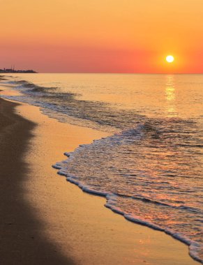 Güneş sakin bir denizin üzerinde doğuyor, yumuşak, köpüklü dalgalar kumlu bir sahile vuruyor..
