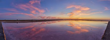 Tuz gölünün durgun, pembe sularına yansıyan renkli bulutlarla canlı bir günbatımı manzarası..