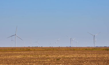 Açık mavi gökyüzünün altında bir rüzgar türbini tarlası. Yenilenebilir enerji ve sürdürülebilir güç üretim kavramı.