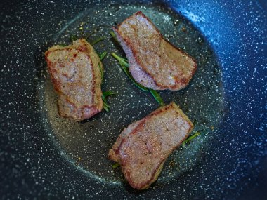 Biberiye filizleriyle kızgın tavada kızartılmış domuz bifteği yakın plan. Et pişirme işlemi sırasında altın-kahverengi bir kabuk geliştiriyor. Ev yapımı yemek hazırlama.