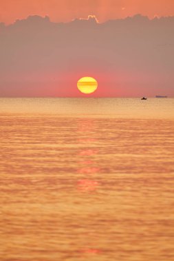 Güneş sakin bir okyanusun üzerinde yükseliyor, yumuşak dalgalar kumlu bir plaja vuruyor..