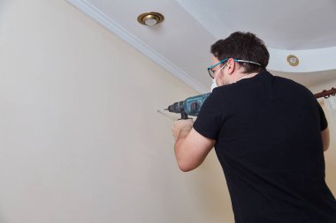 Koruyucu yüz maskesi takan bir işçi duvara delik açmak için elektrikli çekiç matkabı kullanır. Ev yenileme veya inşaat çalışmalarının yakın görüntüsü devam ediyor.