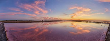 Tuz gölünün durgun, pembe sularına yansıyan renkli bulutlarla canlı bir günbatımı manzarası..