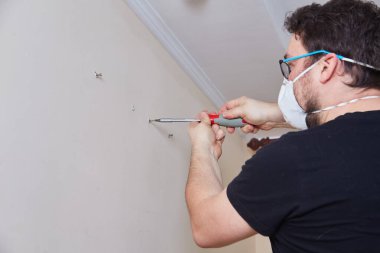 Güvenlik teçhizatı olan bir kişi, bir ev geliştirme veya DIY onarım projesi sırasında pencerenin yakınındaki bir duvara manuel tornavida takıyor. İç oda ayarları.