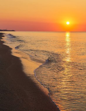 Güneş sakin bir okyanusun üzerinde yükselirken, kıyı şeridinde hafif dalgalar çakıyordu..