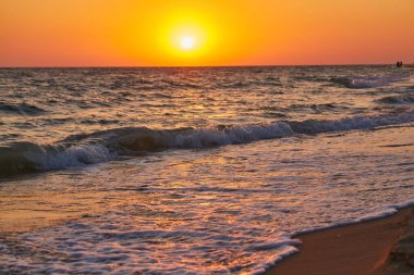 Hafif dalgalar canlı bir altın gün batımı sırasında kumlu bir plajda kıyıya vuruyor. Doğal fotoğraf, sıcak tonlar, arka plan için uygun..