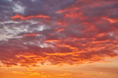 Turuncu ve mavi renkleriyle güzel bir akşam gökyüzü. Yumuşak bulutlar batan güneşle aydınlanır dramatik ve barışçıl bir atmosfer yaratır..