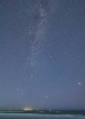 Samanyolu Galaksisi, sakin bir deniz ve kıyı şeridinin üzerindeki gece gökyüzünde görünür..