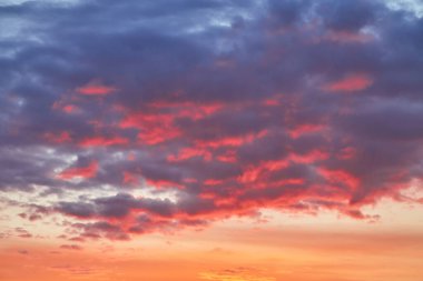 Turuncu ve mavi renkleriyle güzel bir akşam gökyüzü. Yumuşak bulutlar batan güneşle aydınlanır dramatik ve barışçıl bir atmosfer yaratır..