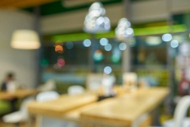 Modern bir kafe ya da restoranın içi bulanık, masaları, sandalyeleri ve asılı lambaları gösteriyor. Yumuşak, odak dışı arkaplan.