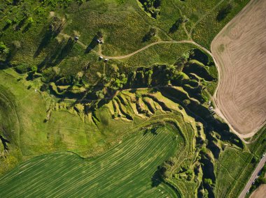 Yukarıdan aşağıya insansız hava aracı görüntüsü, aşınmış tepe ve vadilerin soyut desenlerini yakalar. Kalıplaşmış arka planlar için uygun. Toprak, açıkta kalan toprakla karşıtlığı izler.