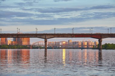Ukrayna 'nın başkenti Kyiv' deki Dnipro Nehri 'ni kapsayan ve arka planda şehir manzarası olan birden fazla köprünün görüntüsü. Köprülerin ve binaların yansımaları suda görülebilir..